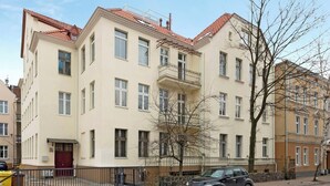 En flervåningsbyggnad med bostäder, balkonger, en grind vid entrén och en parkerad bil.