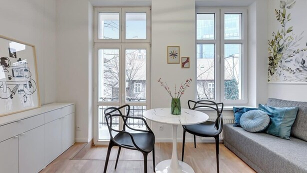 Una cocina moderna con armarios blancos, una mesa de comedor con sillas y un sofá con cojines.