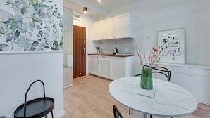 Una cocina moderna con armarios blancos, encimera de mármol y comedor con una mesa redonda y sillas.