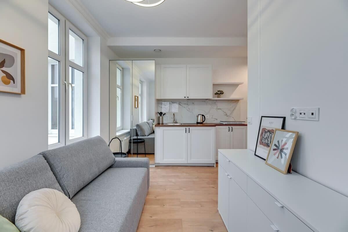 Eine moderne Wohnung mit grauem Sofa, einer Küche mit weißen Schränken und Kunstwerken an den Wänden.