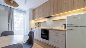Een moderne keuken met houten kastjes, een inbouwoven, een koelkast, en een eethoek met een tafel en stoelen.