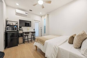 A compact hotel room with a bed, a desk with a microwave, a refrigerator, and a ceiling fan. - Wabi Sabi Studio in EADO (Houston)