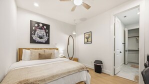 A bedroom with a bed, a ceiling fan, a trash bin, and a door leading to a closet. - Wabi Sabi Studio in EADO (Houston)