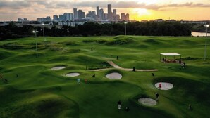 A golf course with bunkers, a tent, and a city skyline in the background. - Wabi Sabi Studio in EADO (Houston)