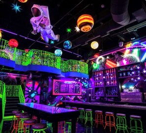 Un área de bar vibrante con luces de neón, una barra, taburetes y un letrero de neón.