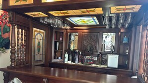 Un espace bar doté d’un comptoir en bois, de verres décoratifs et d’un réfrigérateur.