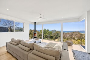 A modern living room with a large sofa, a fireplace, and a view of the ocean. - Stunning Roadknight Residence (Anglesea)