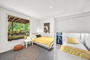 A bedroom with a bed, a small table, a window with a view of greenery, and a wall-mounted decoration.