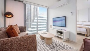 Una habitación de hotel moderna con sofá, una mesa de centro, televisor y cama.