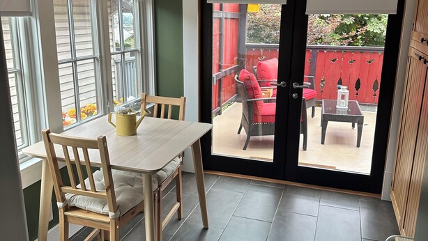Una habitación con una mesa y sillas de comedor, una puerta corrediza de vidrio que da a un patio exterior con valla roja y mobiliario.