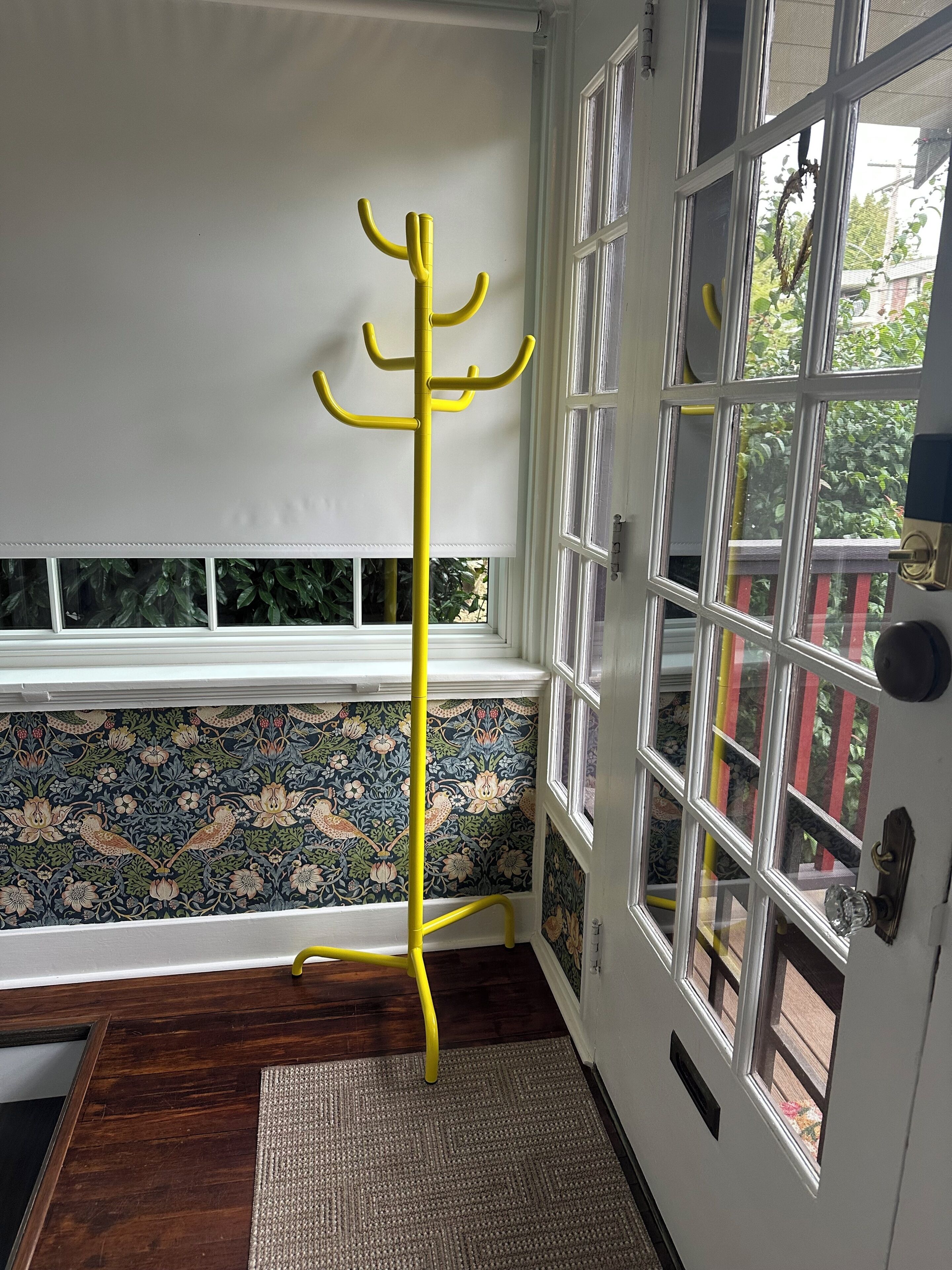 A room with a yellow coat rack, a patterned wallpaper, a wooden floor, and a door with multiple windows.