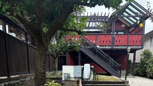 Un patio empedrado con un banco de madera, un árbol y un edificio rojo con escaleras.