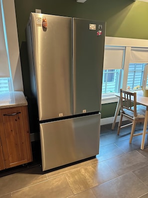 Un refrigerador de acero inoxidable en una cocina con un armario de madera y una ventana con persianas.