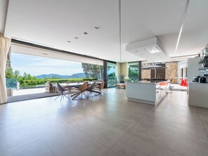 A modern kitchen with a stone backsplash, a dining area with a view, and a large window. - Contemporary Villa – Panoramic Sea View & Rooftop Jacuzzi (Mandelieu-la-Napoule)