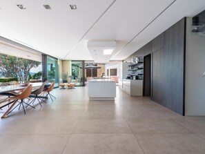 A modern kitchen with a central island, a dining area with a table and chairs, and a view of the outdoors. - Contemporary Villa – Panoramic Sea View & Rooftop Jacuzzi (Mandelieu-la-Napoule)
