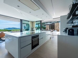 A modern kitchen with a large island, a built-in oven, and a view of the outdoors. - Contemporary Villa – Panoramic Sea View & Rooftop Jacuzzi (Mandelieu-la-Napoule)