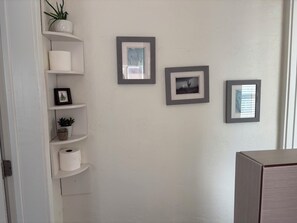 Ein Zimmer mit weißen Wänden, einer Tür und einem Regal mit Pflanzen und gerahmten Bildern.