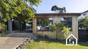 Een modern huis met een houten gevel, grote ramen en een stenen pad dat naar de ingang leidt.