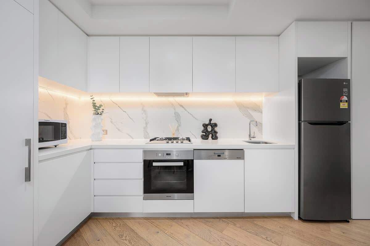 A modern kitchen with white cabinets, a built-in oven, a microwave, and a stainless steel refrigerator.