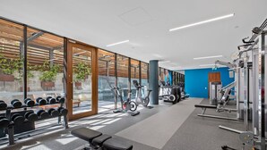 Un gimnasio con equipamiento de ejercicio, una banca y una pared con ventanas.