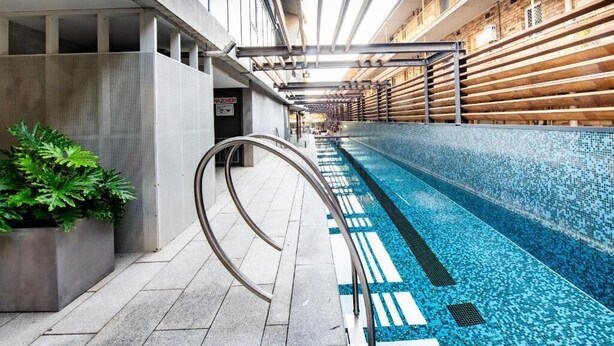 Una piscina con borde de azulejos, barandilla metálica y una planta en maceta.