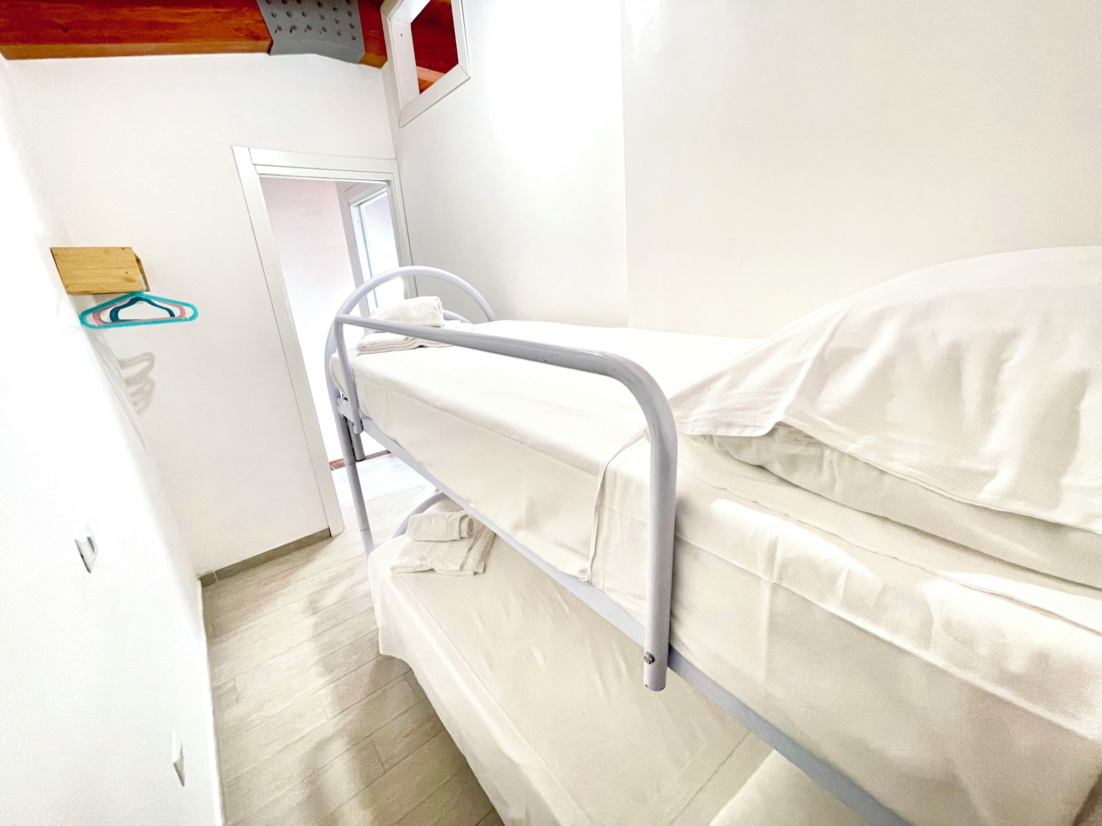 Una cama individual con estructura metálica, ropa de cama blanca y una puerta de madera.