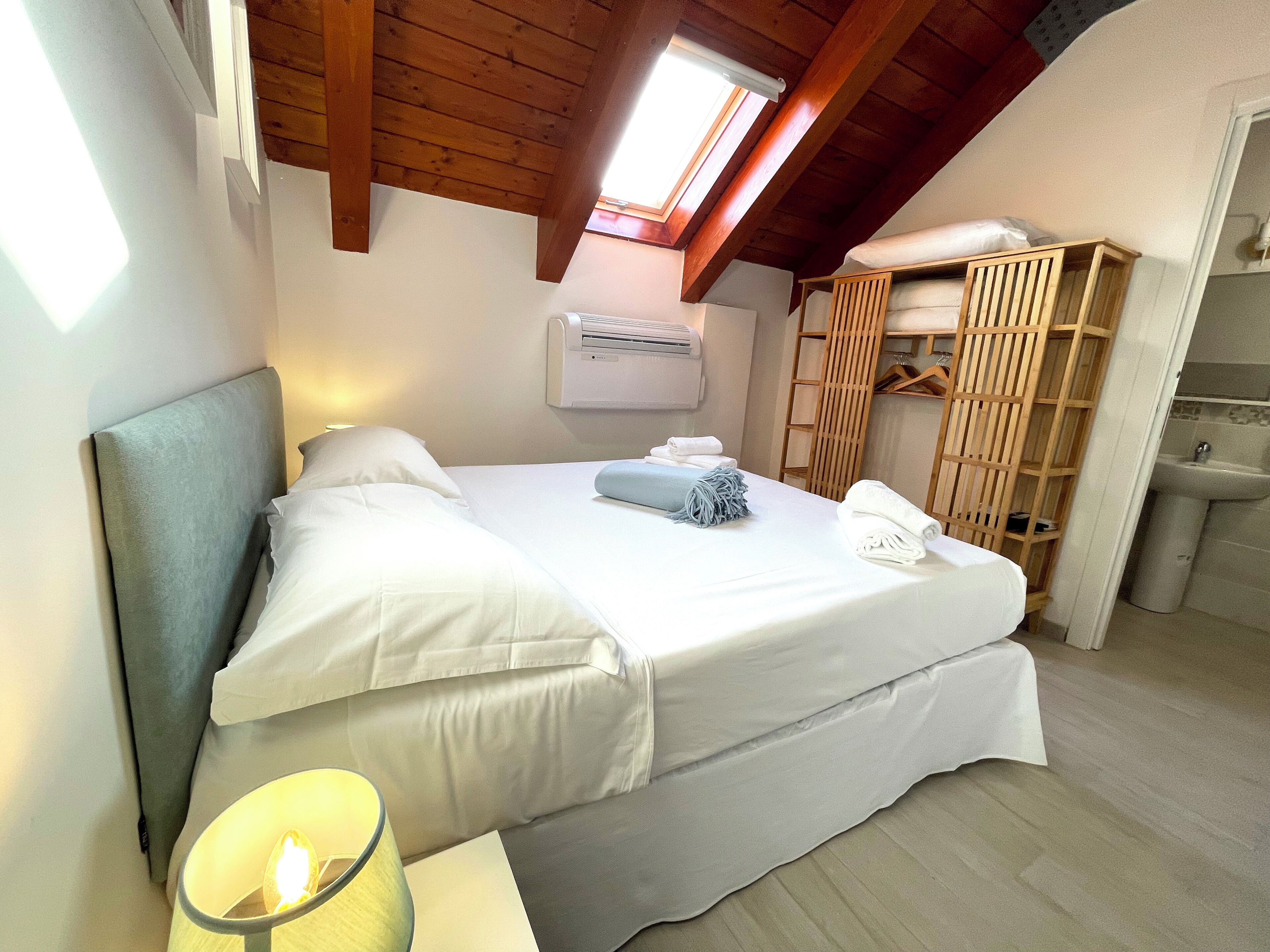 Un dormitorio con cama, lámpara de noche, tragaluz, armario y baño.