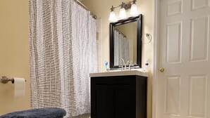 A bathroom with a toilet, sink, mirror, shower curtain, and a door.