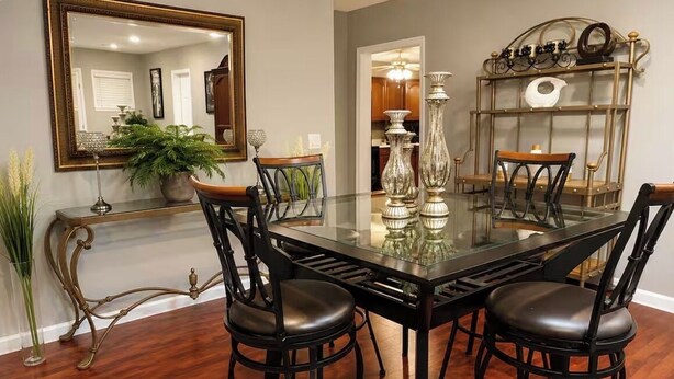 A dining area with a glass table, black chairs, a mirror, and a decorative shelf.