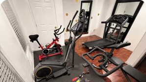 A home gym with an elliptical, a stationary bike, a treadmill, and a bench.