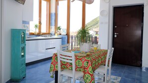 Un coin repas avec une table dressée pour deux personnes, une cuisine en arrière-plan et une vue sur l’extérieur.