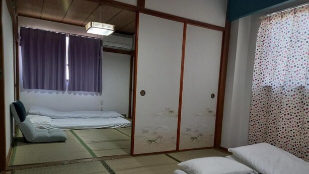 Una habitación tradicional japonesa con suelo de tatami, futón, pantalla shoji y puertas correderas.