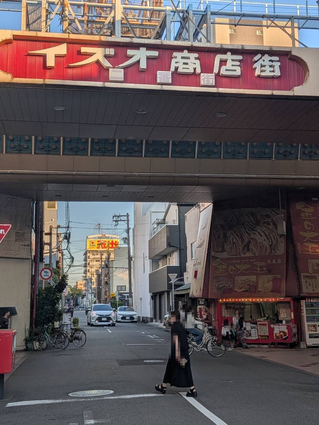 A street with a pedestrian crossing under an overpass. There are bicycles parked on the side, and a few cars on the road.