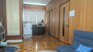 Una habitación con sofá, alfombra estampada, kitchenette con microondas y una puerta con un cartel.
