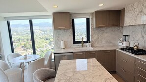 A modern kitchen with marble countertops, a central island, and a view of a cityscape. - Luxury Living at Aqua | Pool, Spa, Golf Sim plus Downtown Kelowna & Lake Views (Kelowna)