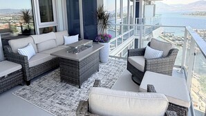 A balcony with wicker furniture, a large window, and a view of the water. - Luxury Living at Aqua | Pool, Spa, Golf Sim plus Downtown Kelowna & Lake Views (Kelowna)