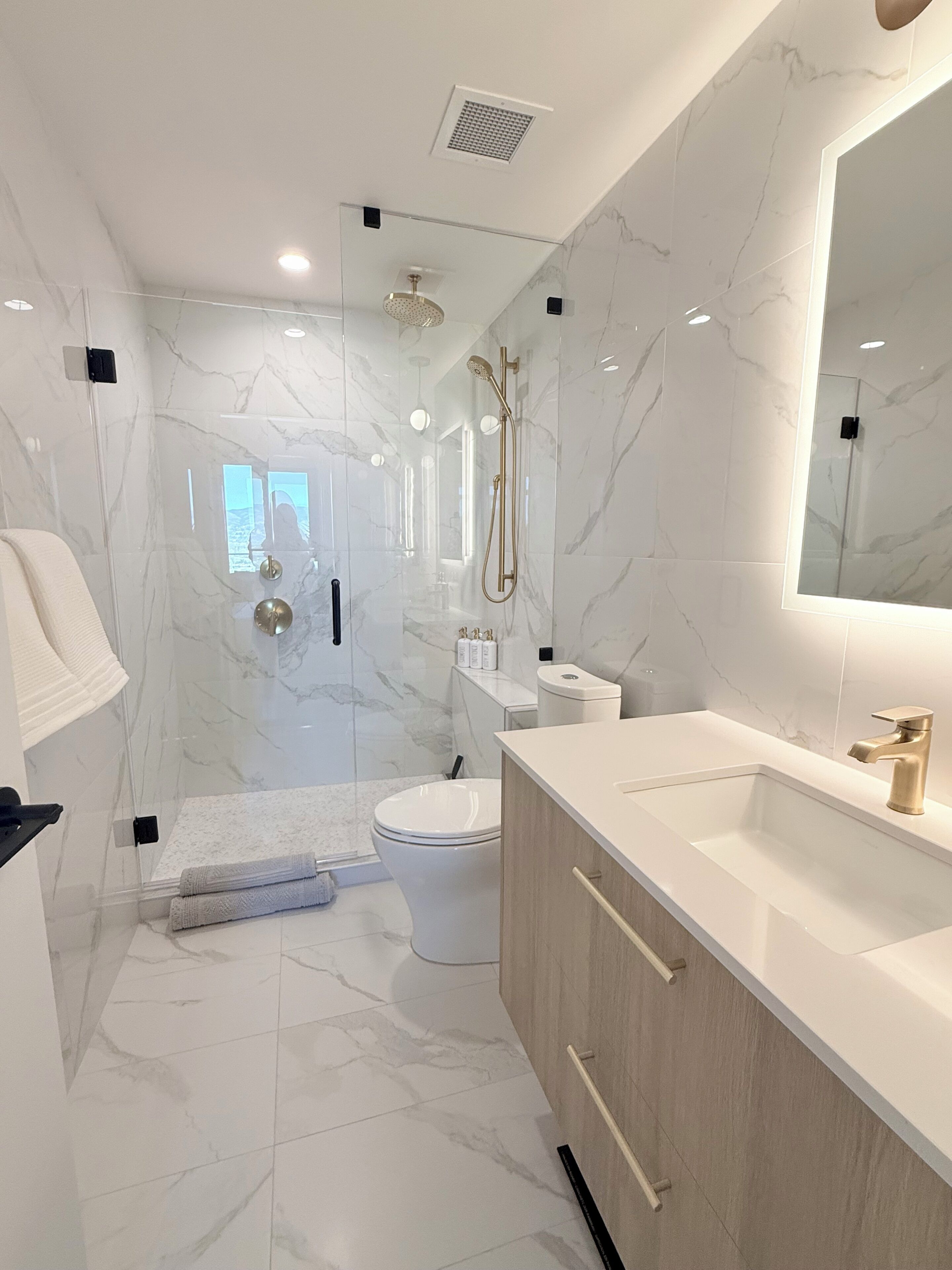 Een moderne badkamer met een douche met glazen wand, een toilet en een wastafelmeubel met wastafel en spiegel.