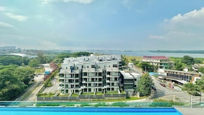 Un edificio moderno de varios pisos con techo plano, rodeado de vegetación y una masa de agua al fondo.