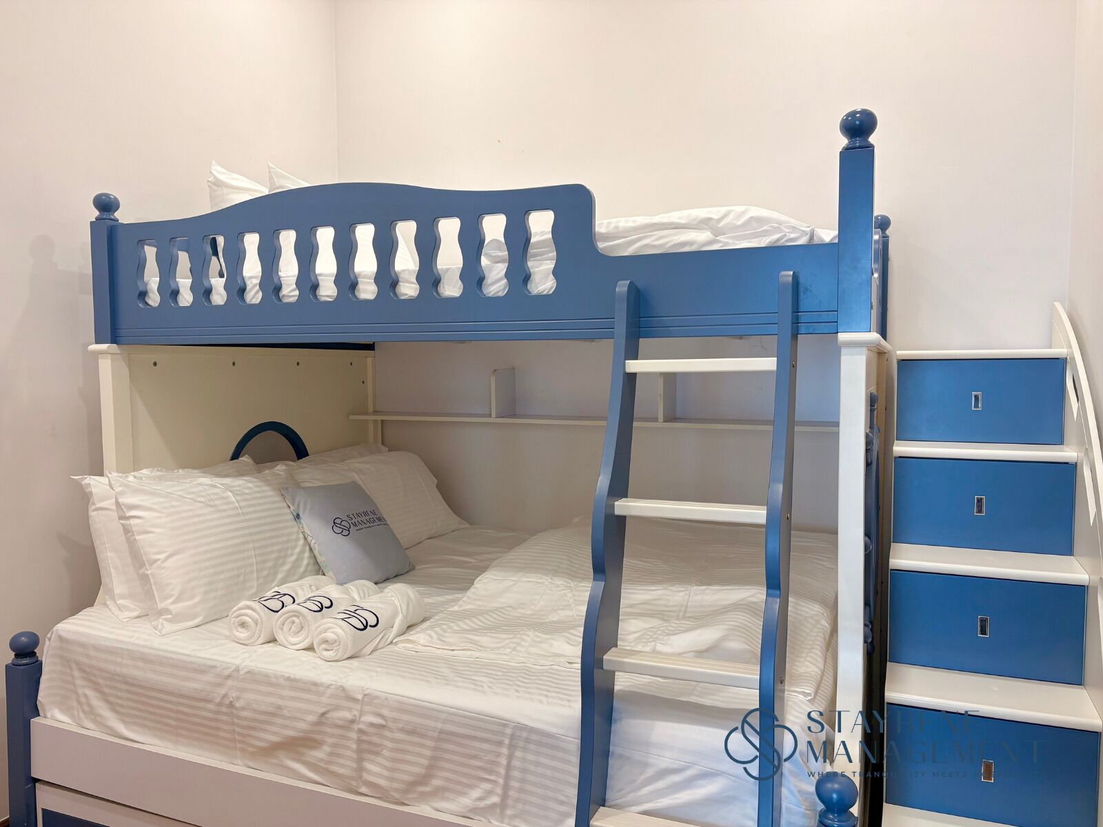 A bunk bed with a ladder, white bedding, and a pillow with a logo.
