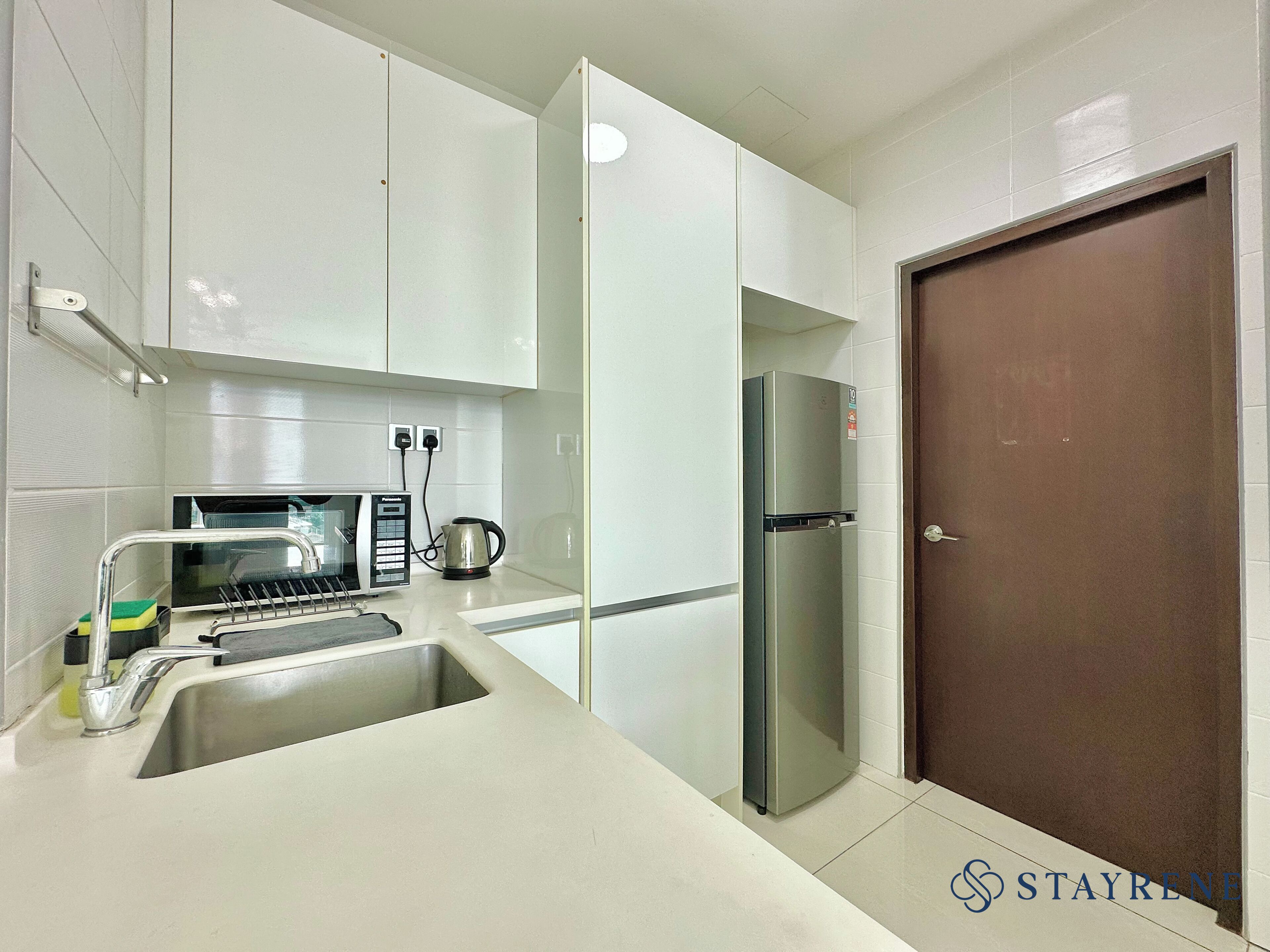 A modern kitchen with white cabinets, a stainless steel sink, a kettle, a refrigerator, and a microwave.