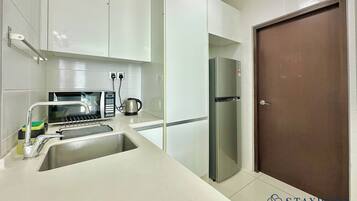 A modern kitchen with white cabinets, a stainless steel sink, a kettle, a refrigerator, and a microwave.