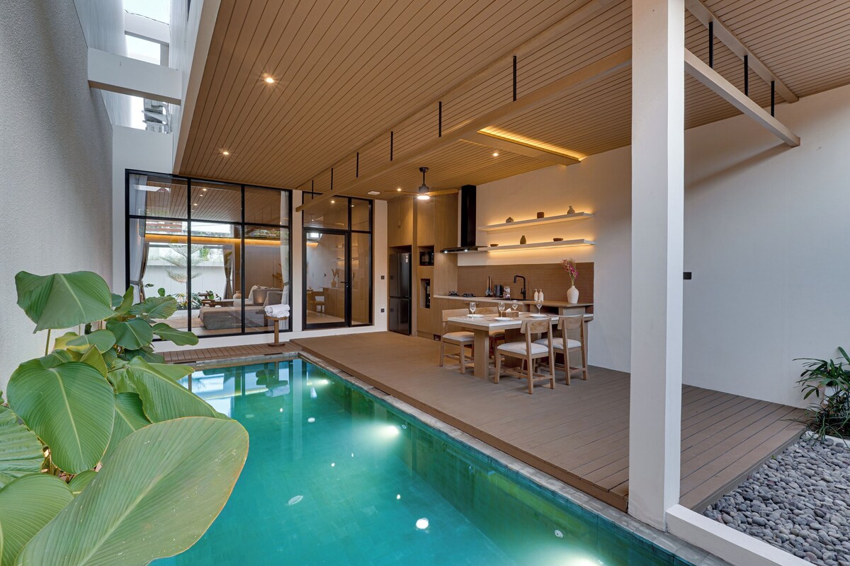 A modern interior with a swimming pool, wooden flooring, and a dining area with a table and chairs.