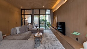 Ein modernes Wohnzimmer mit einer Couch, einem Couchtisch, einem Fernseher und Blick auf einen Garten durch große Fenster.