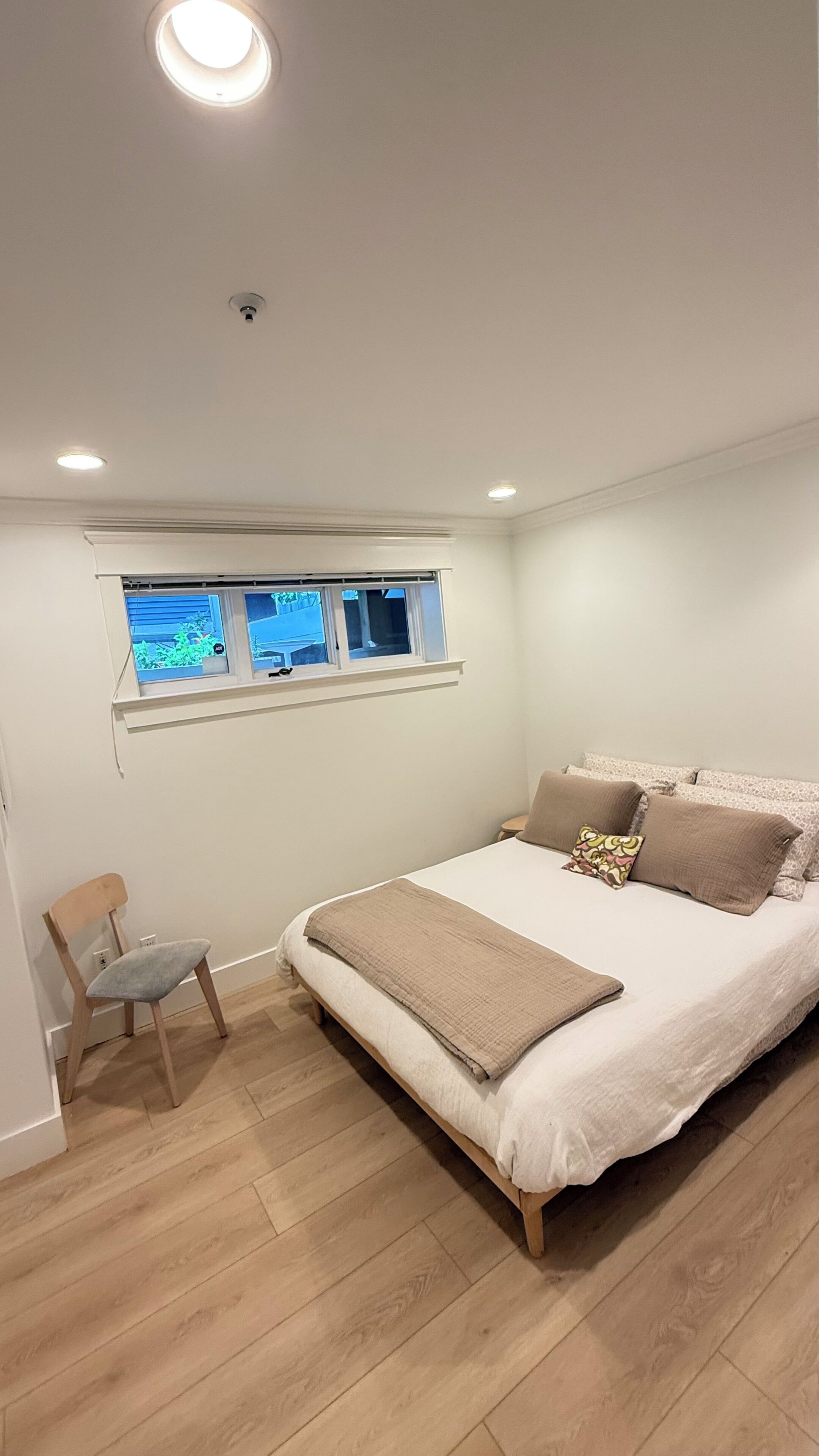 A bedroom with a bed, a chair, a window, and a ceiling light.