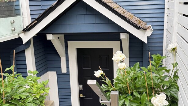 Een huis met een zwarte deur, een klein portaal en een betonnen pad naar de ingang.