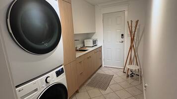A laundry room with stacked washers and dryers, a microwave, and a door leading to another room.