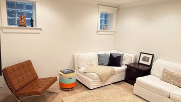 A living room with a brown chair, a white sofa, a beige rug, and a small table with a picture frame.