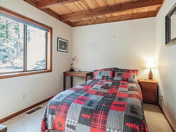 A bedroom with a large bed, a nightstand, a lamp, and a window with a view of trees.
