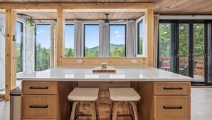 A kitchen with a large island, wooden cabinets, and a view of greenery. - Scandinavian-Modern Couples Retreat w/ Sauna, Hot Tub & Cold Plunge (Stow)