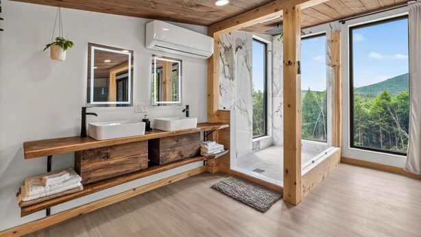 A modern bathroom with wooden beams, two sinks, a mirror, and a large window with a view of greenery. - Scandinavian-Modern Couples Retreat w/ Sauna, Hot Tub & Cold Plunge (Stow)